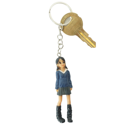 Keychain with a figurine of a person wearing a blue sweater and skirt, attached to a key on a white background.