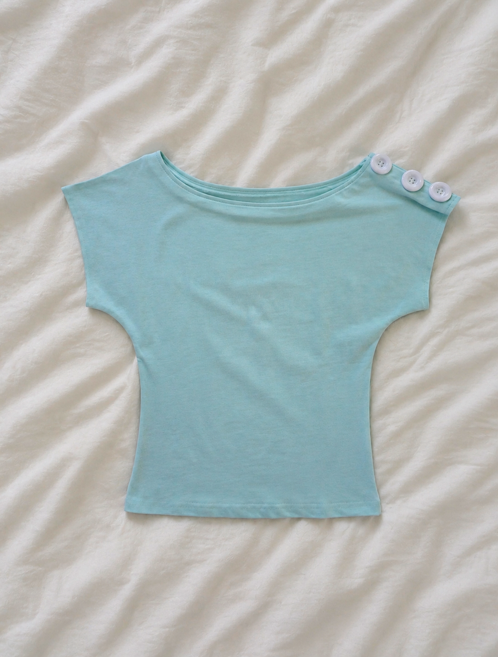 Light blue crop top with button details on a beige surface