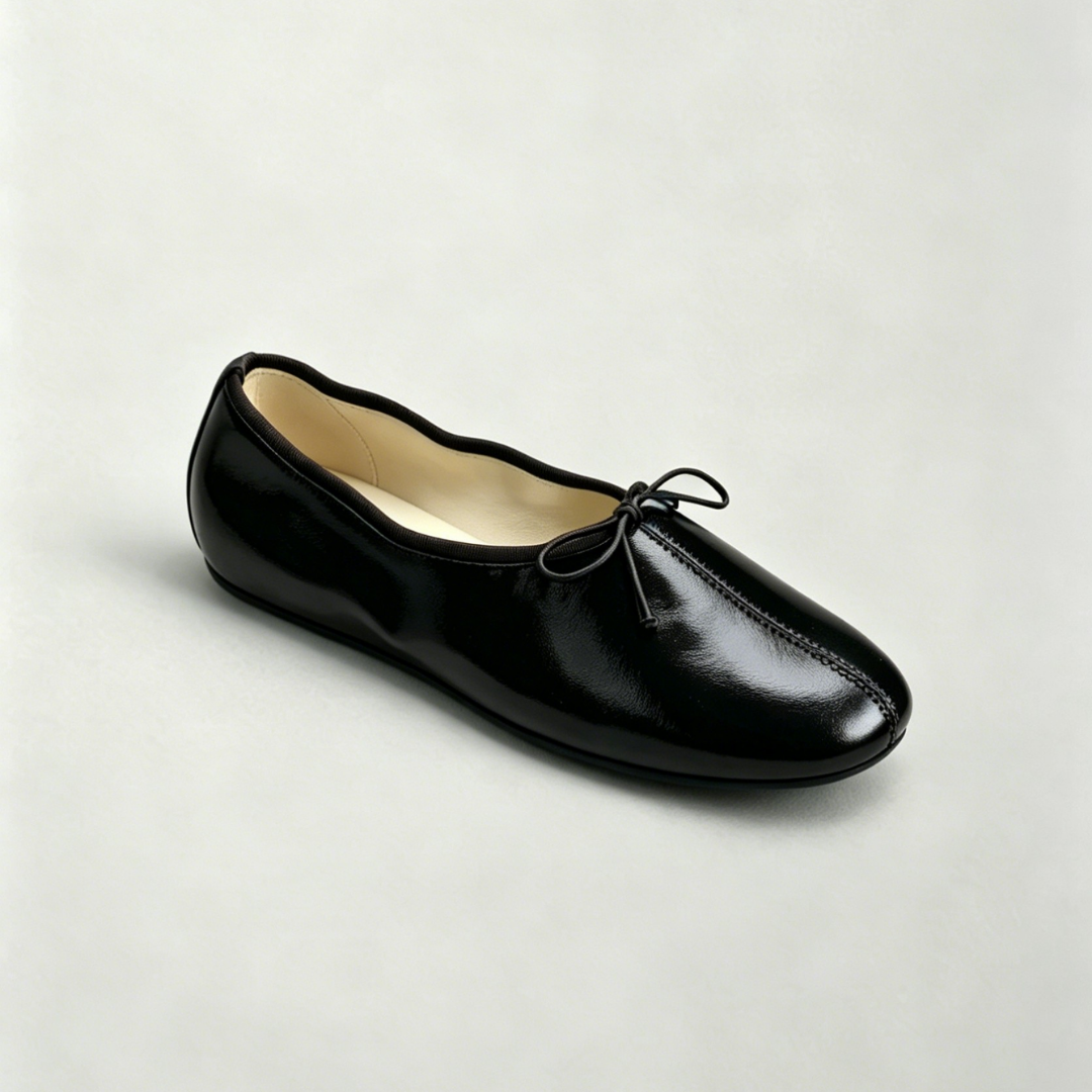Black leather flat shoe with a bow on a light gray background