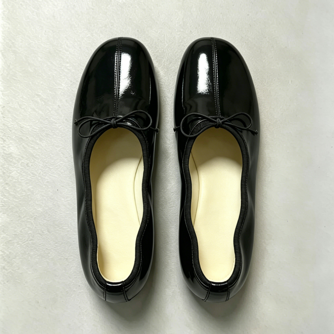 Pair of black patent leather shoes with bow details on a light gray background