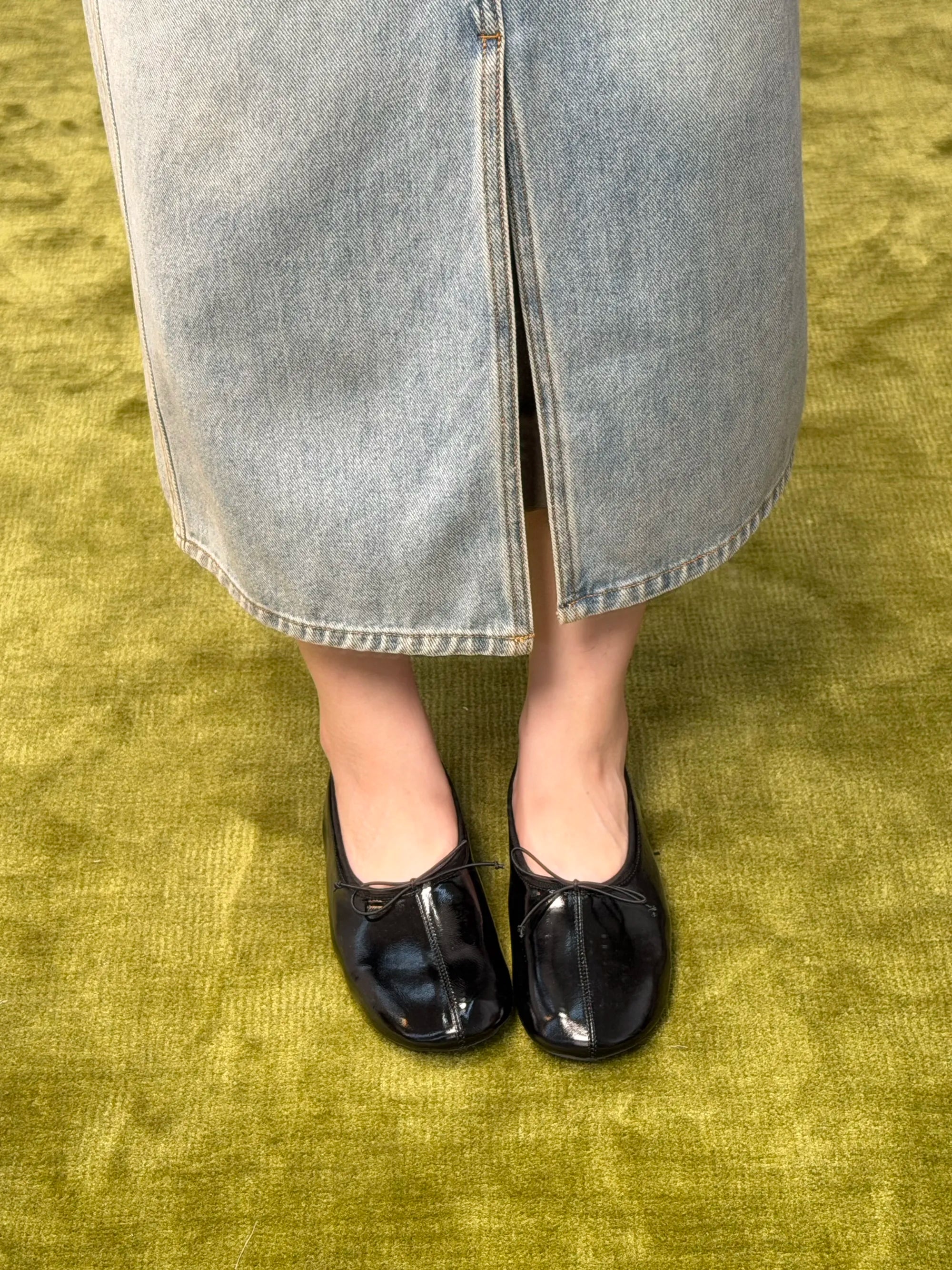 Person wearing black shoes and a light blue denim skirt on a green carpet.