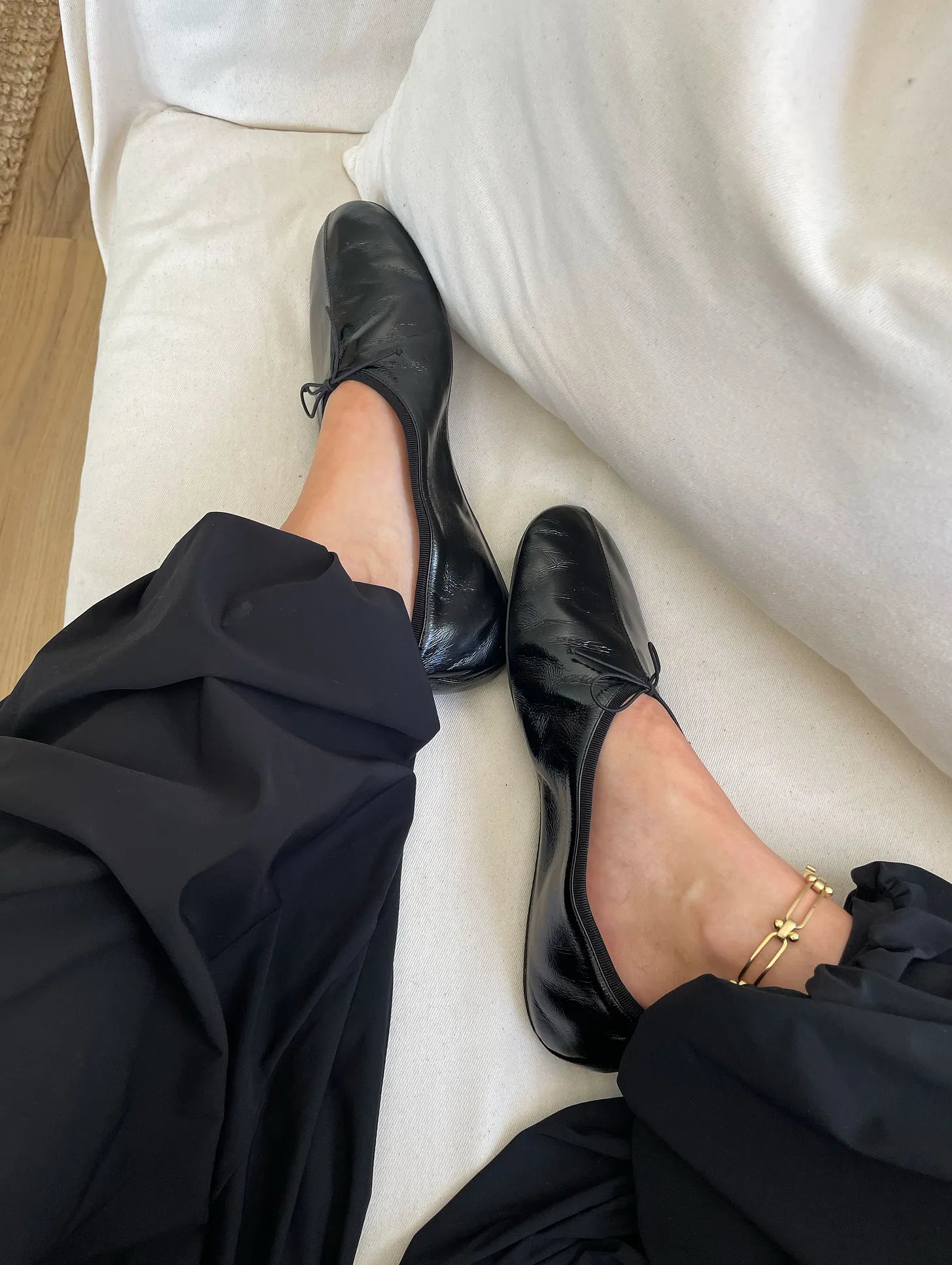 Person wearing black shoes and pants sitting on a white surface.