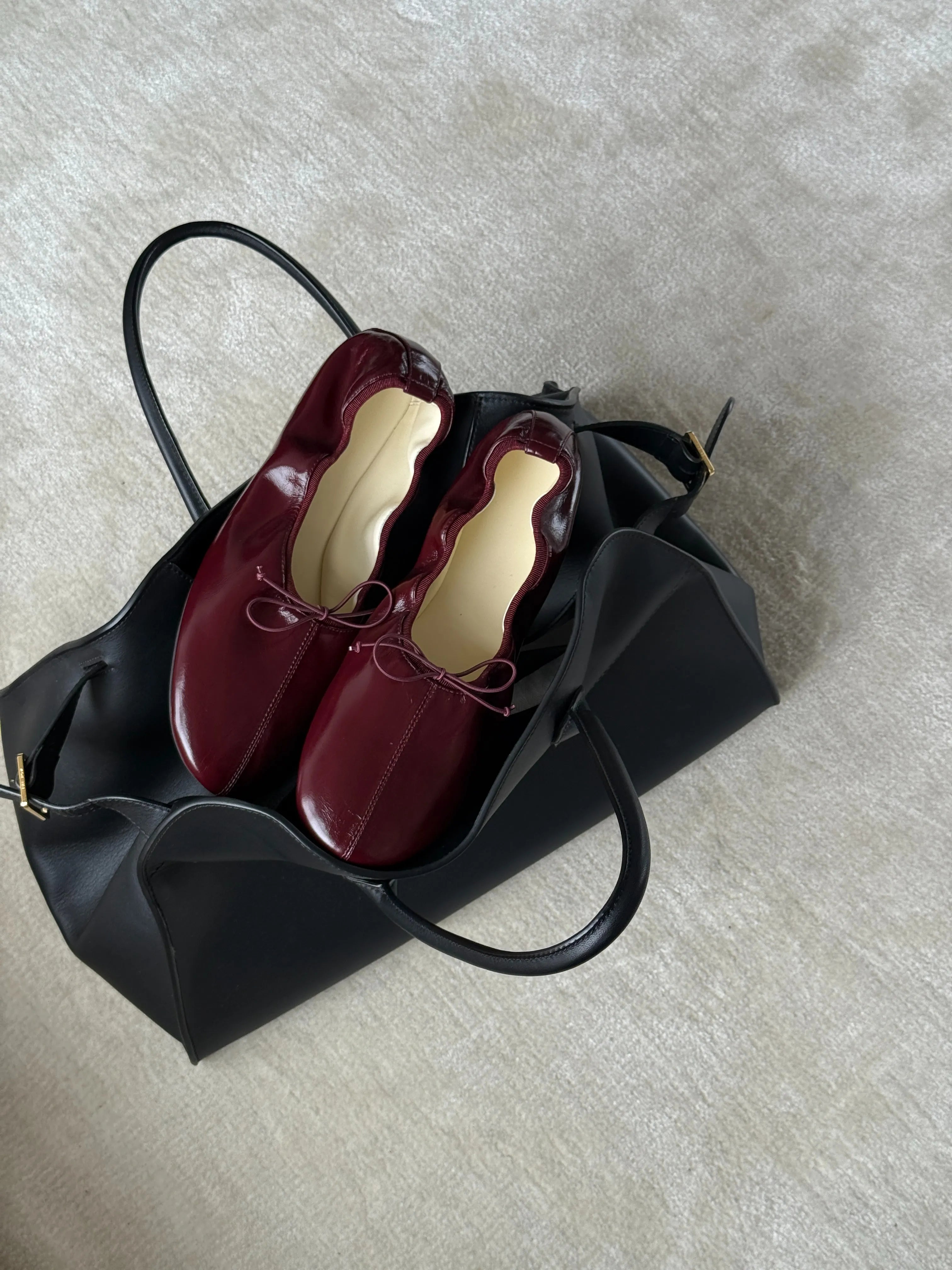 Pair of maroon shoes inside a black handbag on a light gray surface