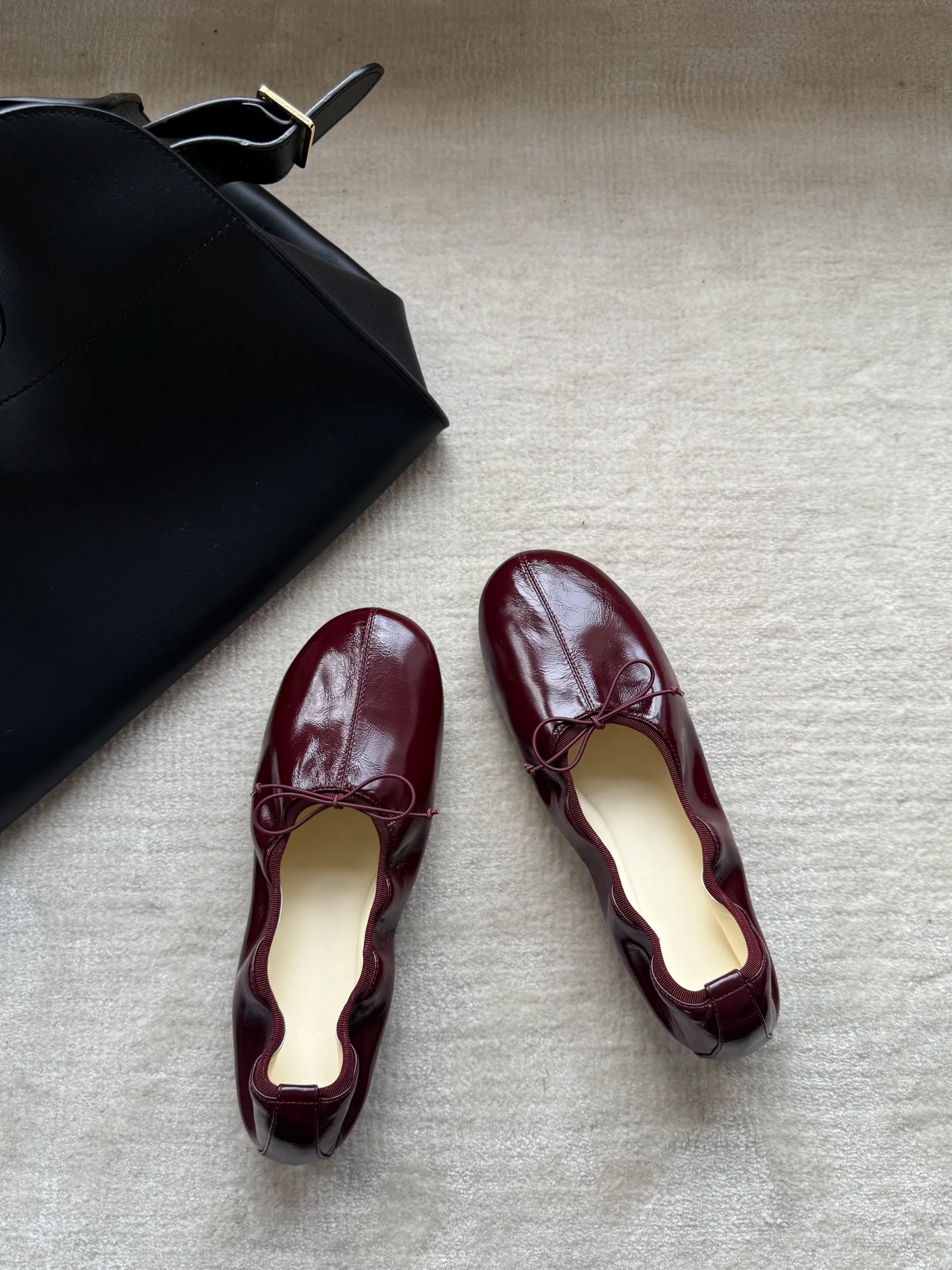 Pair of maroon loafers on a textured surface with a black handbag.