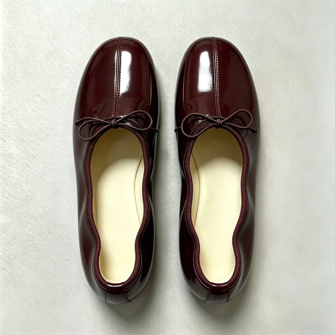 Pair of maroon shoes with bow details on a light gray background