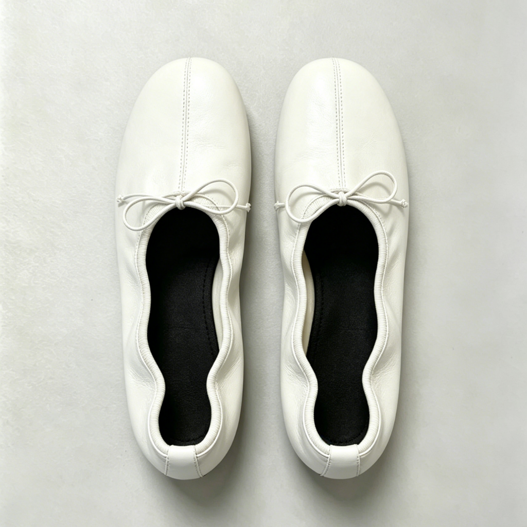 Pair of white ballet flats with ribbons on a light gray background