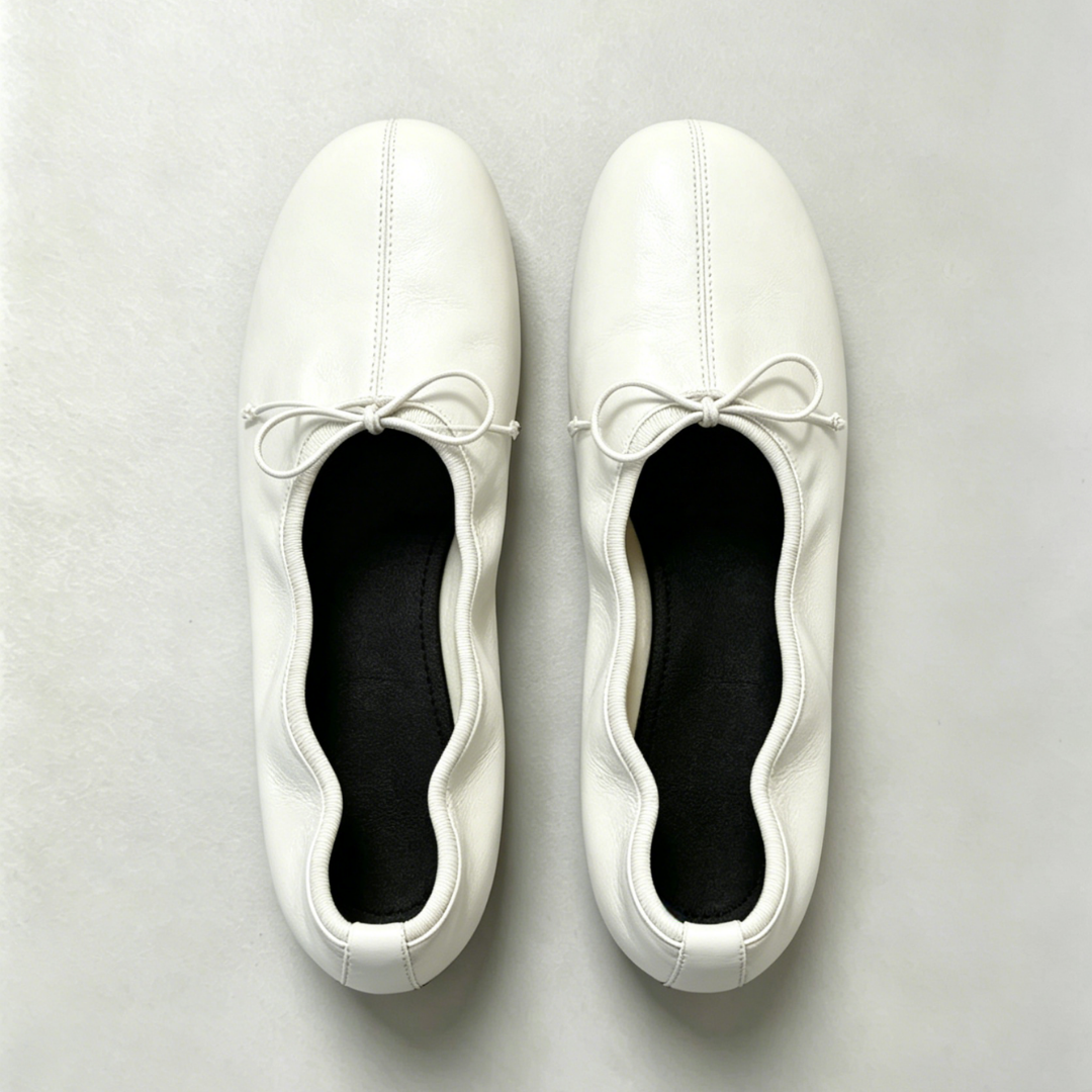 Pair of white ballet flats with ribbons on a light gray background