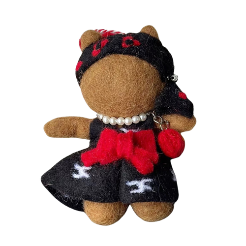 Small plush toy bear wearing a black outfit with red accents on a white background
