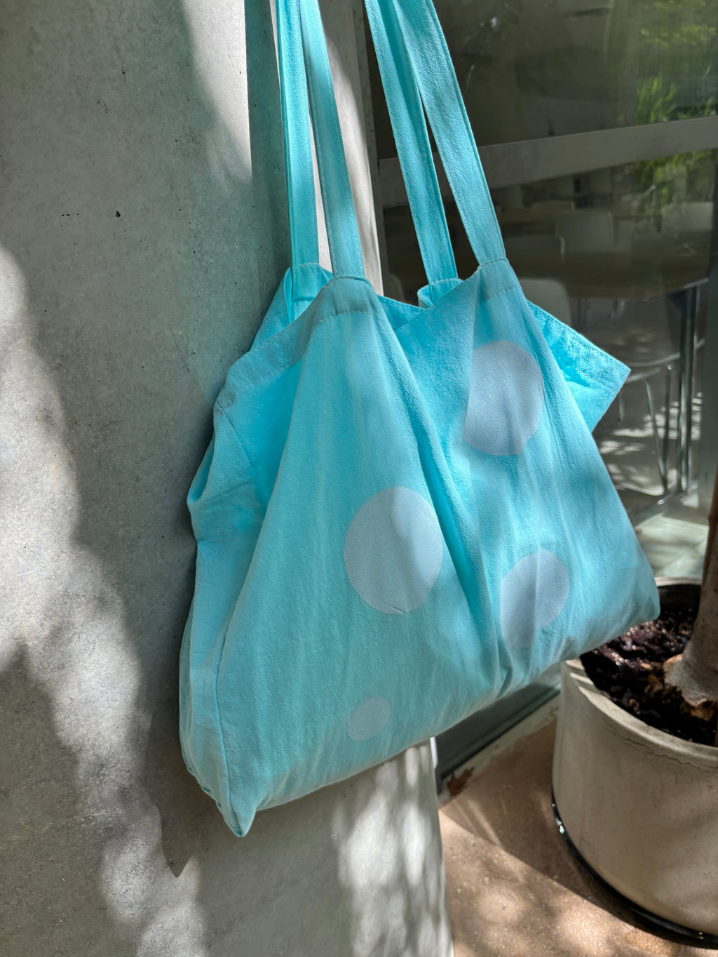 Light blue tote bag with white polka dots hanging on a metal railing.