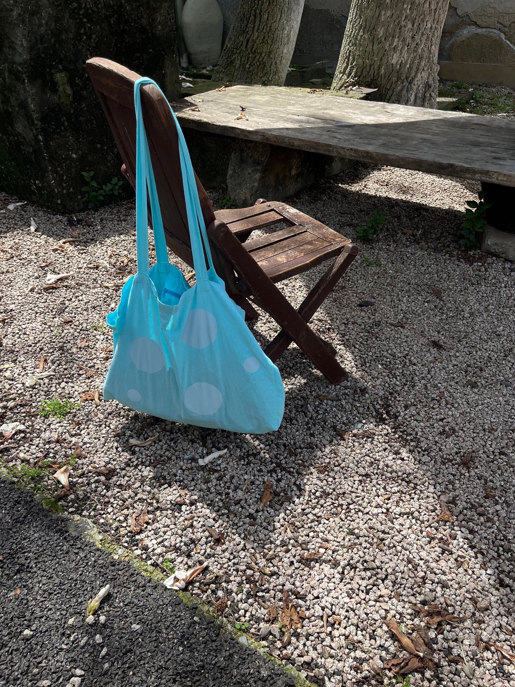 Light blue bag with white polka dots on a wooden chair outdoors.