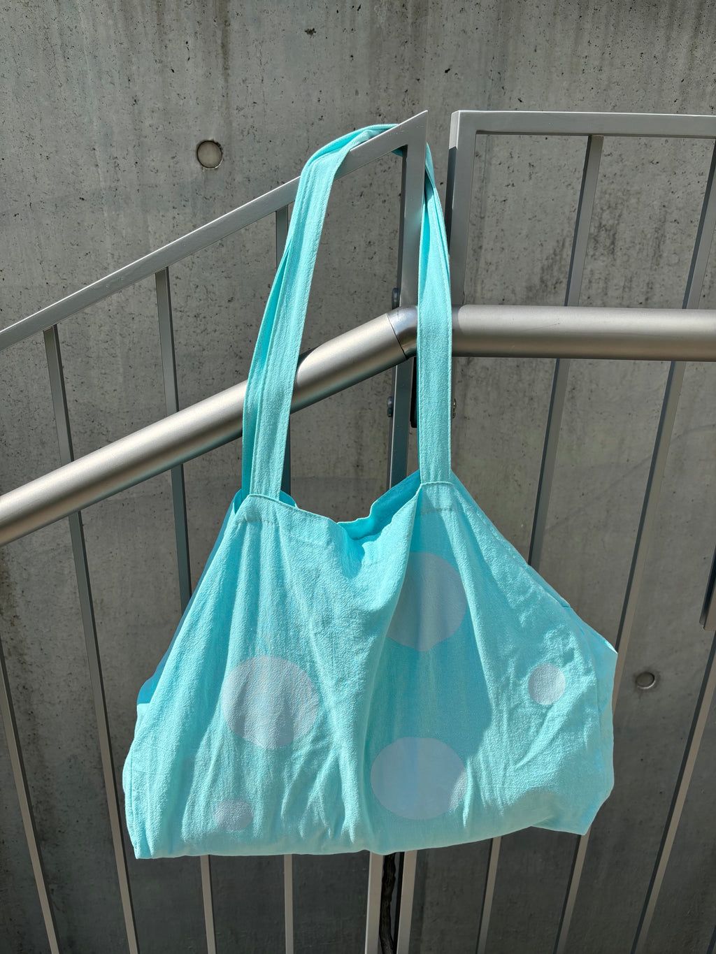Light blue tote bag with white polka dots hanging on a metal railing.