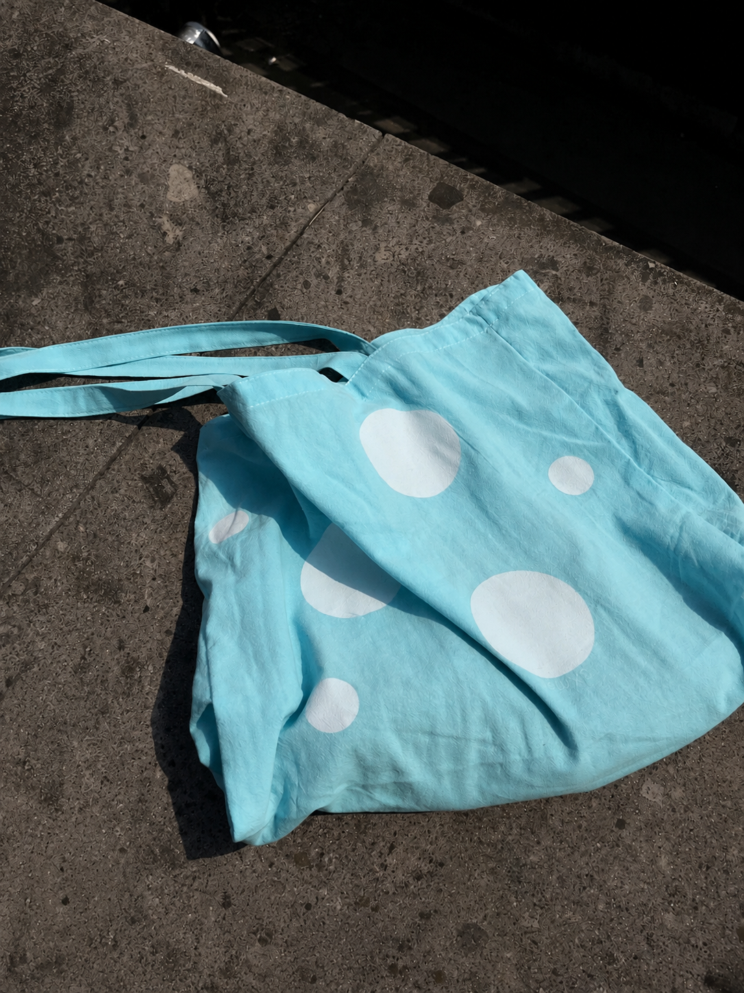 Light blue tote bag with white polka dots on a concrete surface