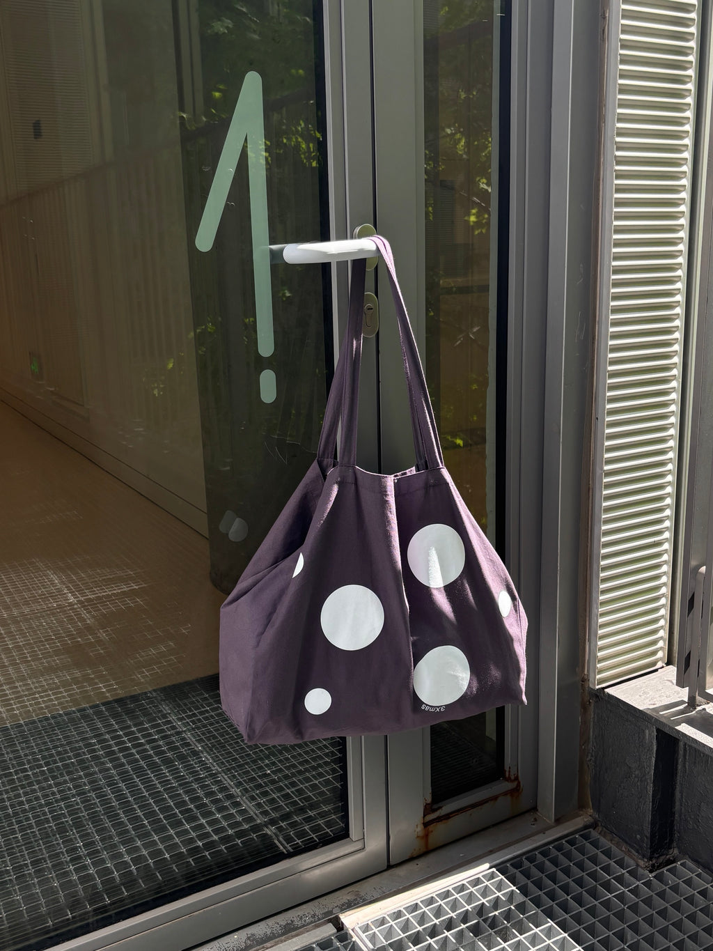 Purple bag with white polka dots hanging on a door handle.