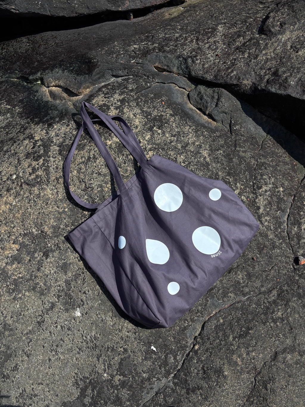 Black tote bag with white polka dots on a rocky surface
