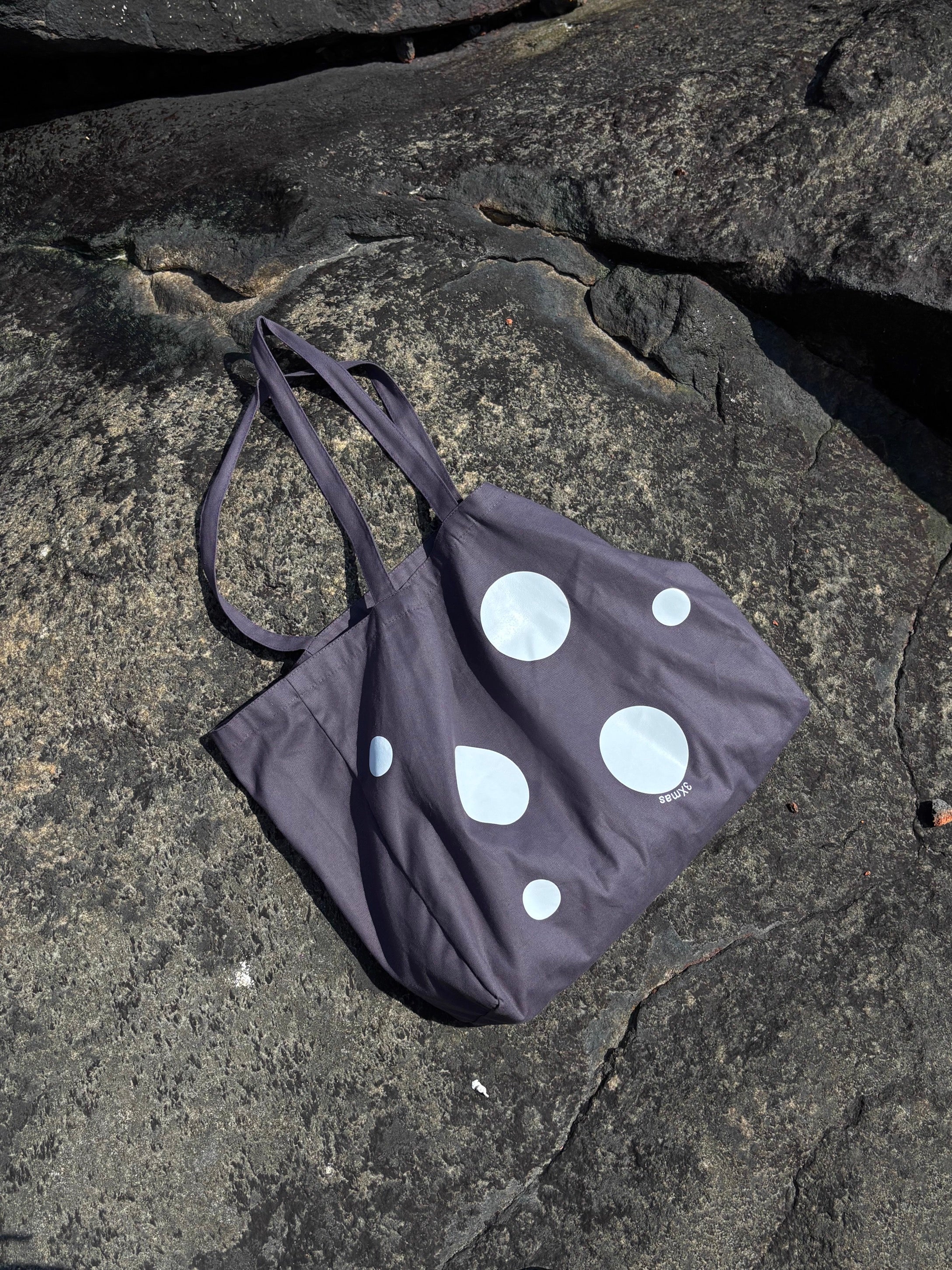 Black tote bag with white polka dots on a rocky surface