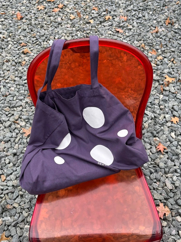 Navy blue bag with white polka dots on a red chair outdoors.