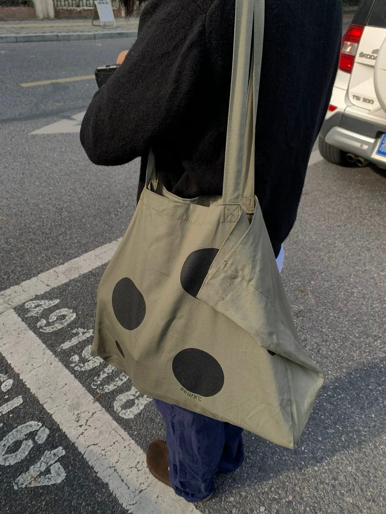 Person holding a beige tote bag with black polka dots on a street.