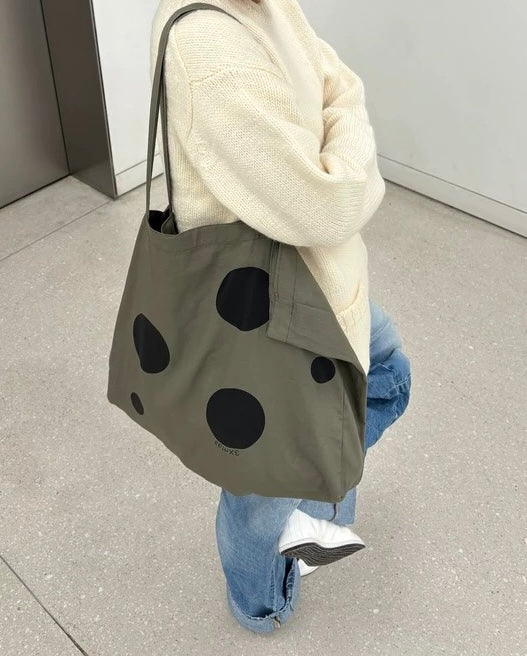 Person wearing a beige sweater and blue jeans, holding a green tote bag with black polka dots.