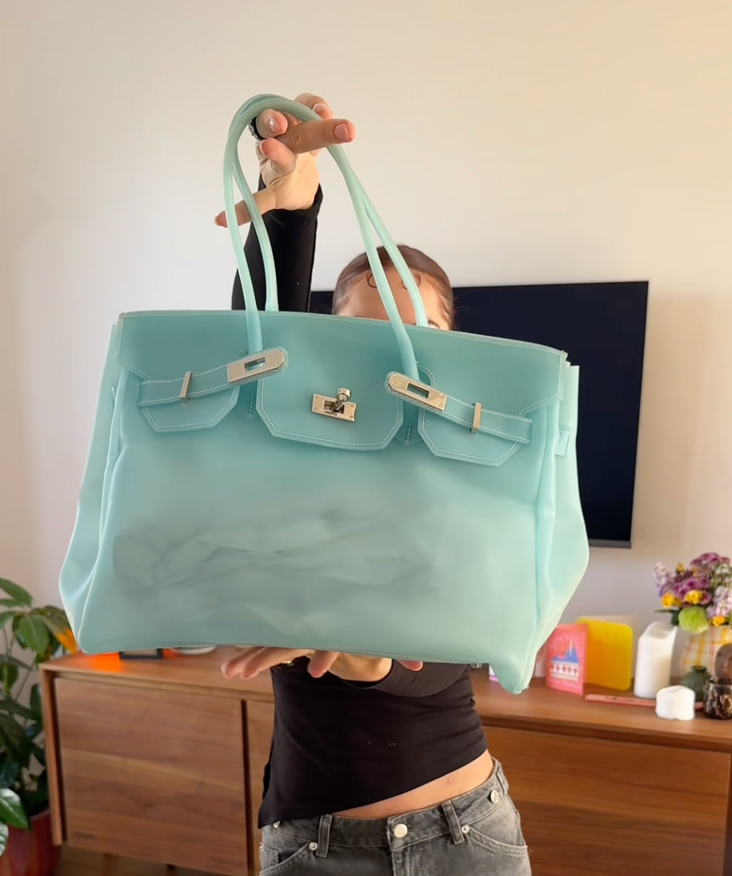 Person holding a light blue handbag with a visible brand logo in an indoor setting.