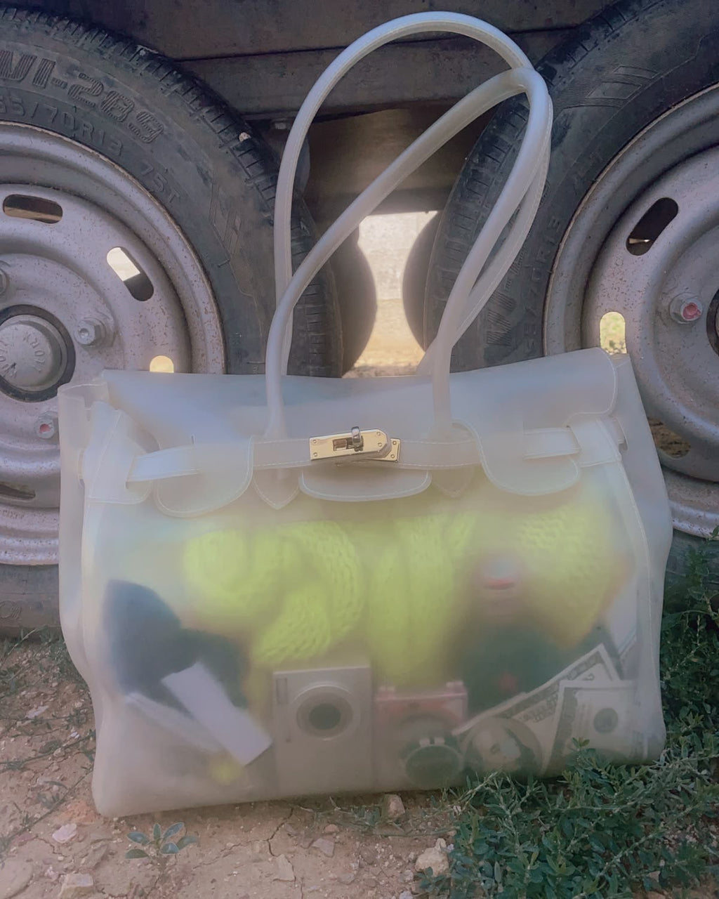 Clear handbag with visible contents against a vehicle wheel background